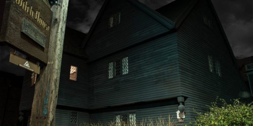 The Witch house, a dark, matt black peaked timber house with small illuminated windows, features in this night time photo.