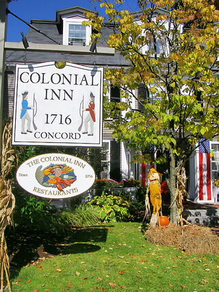 photo shows the front of the colonial inn as well as the sign for the lodging itself. on it are two colonial era war soldiers facing each other.
